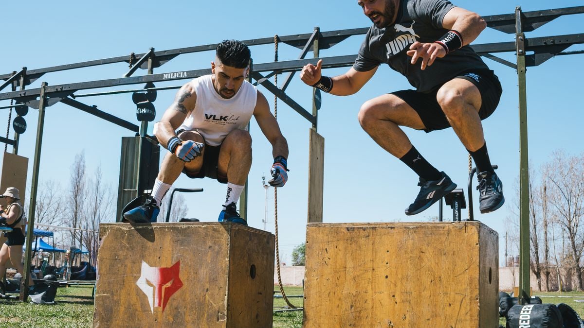 Two men demonstrating intense box jump exercises at an outdoor fitness event.